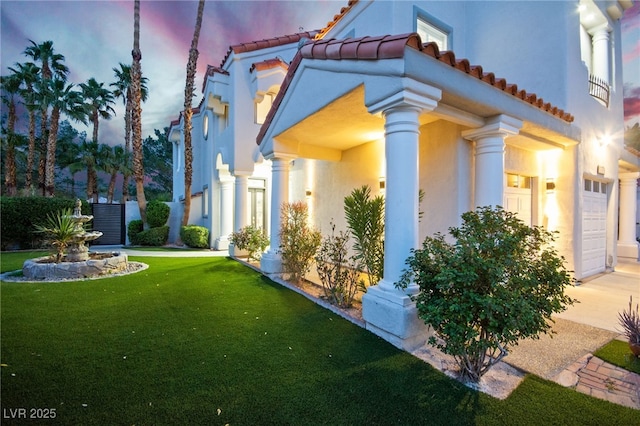 view of side of home featuring an attached garage, a yard, stucco siding, concrete driveway, and a tiled roof