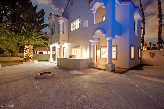 view of front of property with stucco siding, fence, an outdoor fire pit, an outdoor kitchen, and a patio area