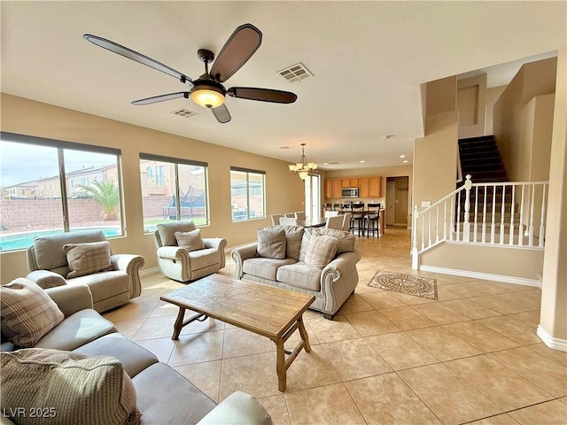 living room with stairway, light tile patterned flooring, ceiling fan with notable chandelier, and visible vents