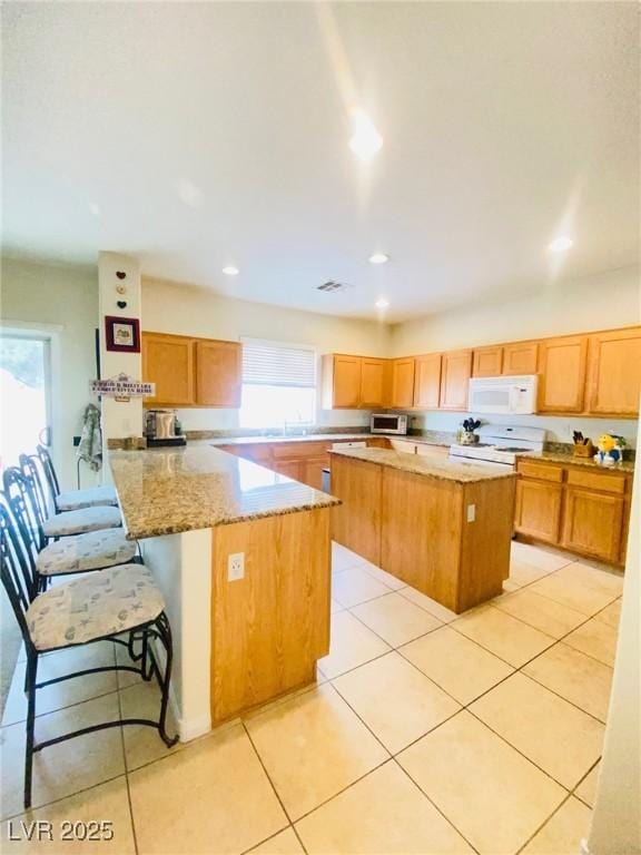 kitchen with a peninsula, a healthy amount of sunlight, white microwave, and a kitchen island