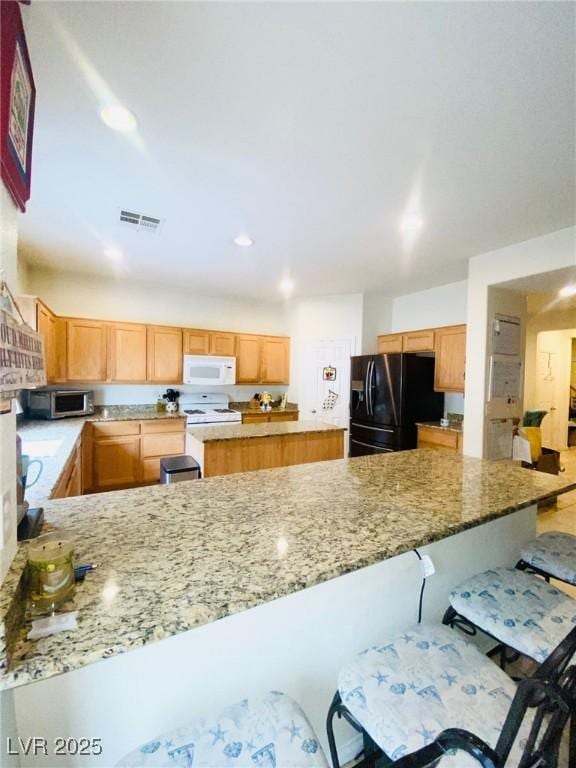 kitchen featuring visible vents, black fridge, stainless steel microwave, a peninsula, and white microwave