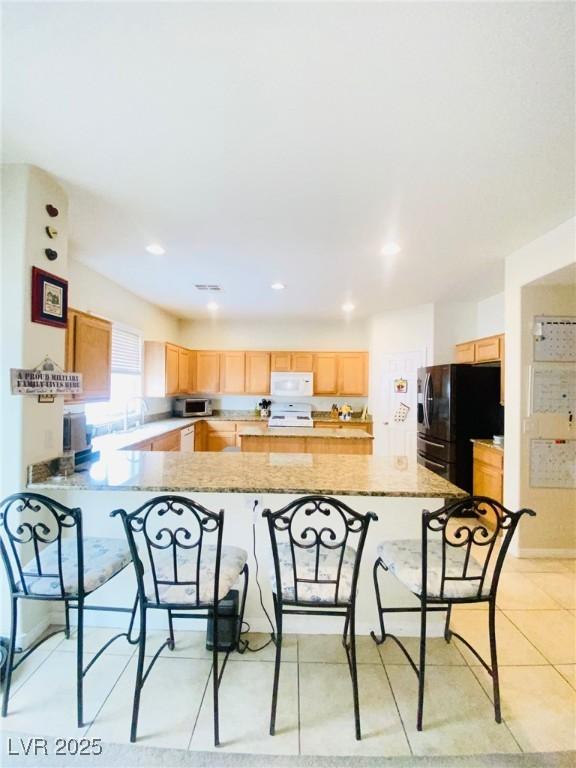 kitchen with white microwave, light brown cabinets, and freestanding refrigerator