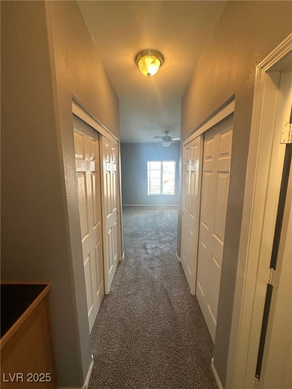 hallway featuring baseboards and dark colored carpet