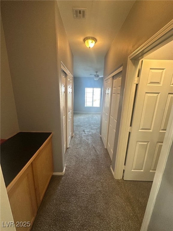 hallway featuring baseboards, visible vents, and dark carpet