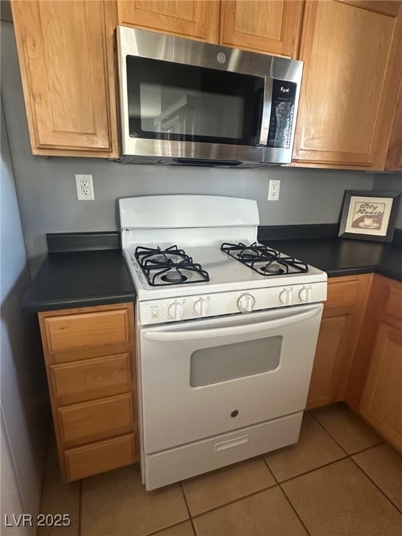 kitchen featuring stainless steel microwave, white gas stove, dark countertops, and light tile patterned flooring