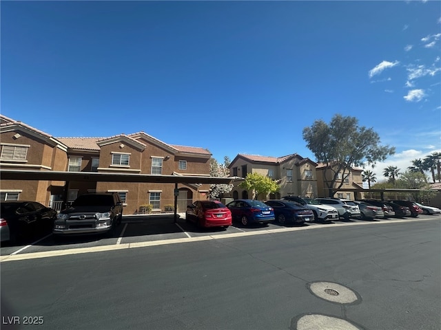 townhome / multi-family property with a tiled roof, covered and uncovered parking, a residential view, and stucco siding