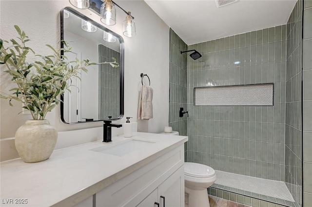 bathroom with a tile shower, visible vents, toilet, and vanity