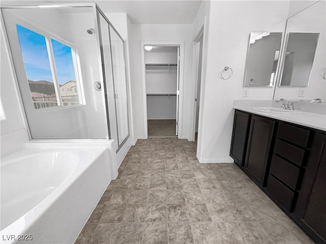 full bathroom with a shower stall, a walk in closet, baseboards, a bath, and vanity