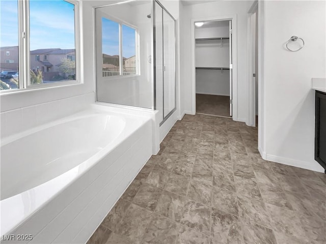 bathroom featuring a garden tub, a stall shower, baseboards, a spacious closet, and vanity