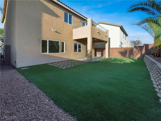 rear view of property with fence, stucco siding, a lawn, a balcony, and a patio