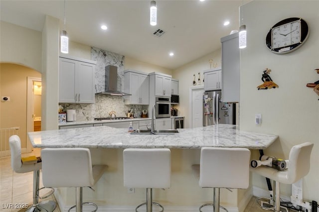 kitchen featuring a breakfast bar area, stainless steel appliances, wall chimney range hood, and a sink