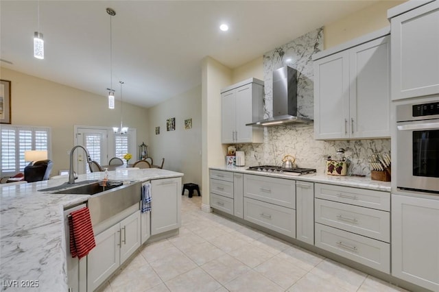 kitchen with lofted ceiling, decorative backsplash, appliances with stainless steel finishes, wall chimney range hood, and decorative light fixtures