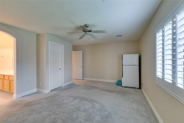 interior space with baseboards, arched walkways, light colored carpet, and ceiling fan