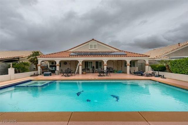 rear view of property featuring stucco siding, a pool with connected hot tub, roof mounted solar panels, a patio area, and a tiled roof