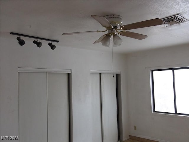 unfurnished bedroom with visible vents, two closets, ceiling fan, rail lighting, and a textured ceiling