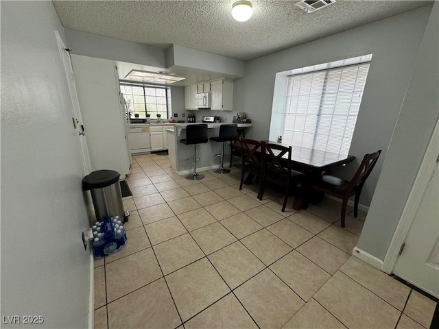 dining area featuring light tile patterned floors, visible vents, a textured ceiling, and baseboards