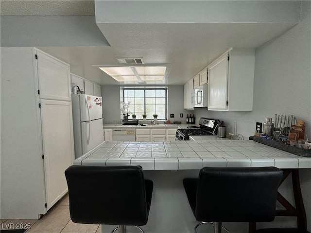 kitchen with visible vents, tile counters, a peninsula, white cabinets, and white appliances