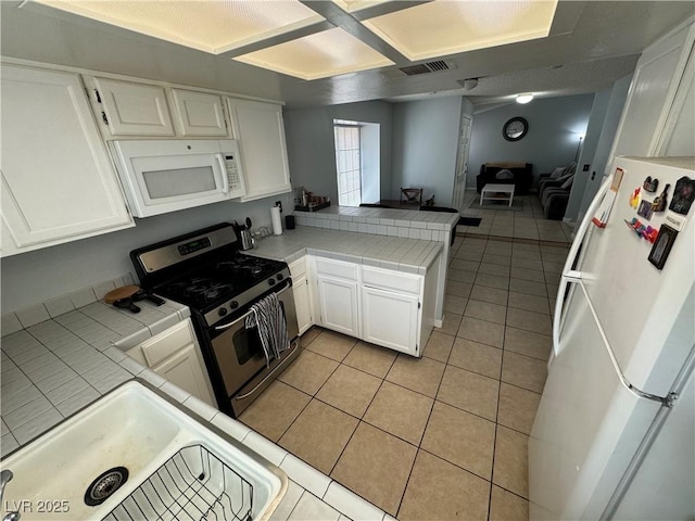 kitchen featuring light tile patterned flooring, white appliances, a peninsula, and tile counters