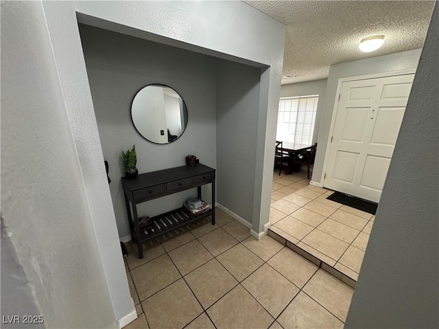 hallway featuring baseboards, a textured ceiling, and light tile patterned flooring