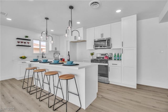 kitchen featuring visible vents, a kitchen bar, open shelves, white cabinetry, and appliances with stainless steel finishes