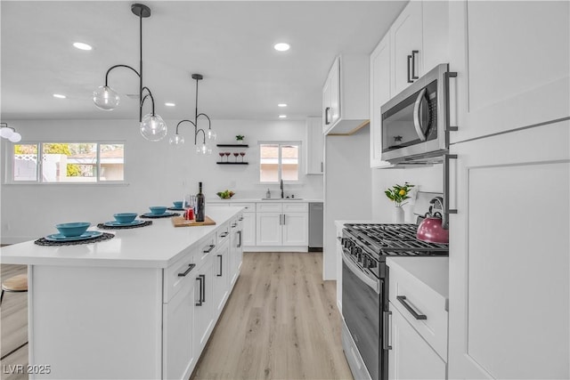 kitchen with light wood-type flooring, light countertops, appliances with stainless steel finishes, white cabinets, and a sink