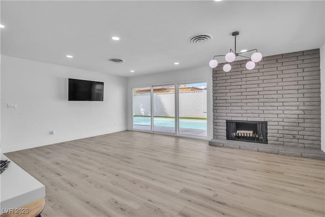 unfurnished living room with a brick fireplace, recessed lighting, wood finished floors, and visible vents