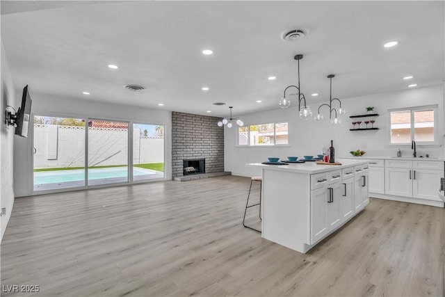 kitchen featuring light wood finished floors, visible vents, a brick fireplace, and white cabinetry