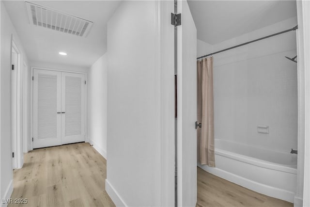 corridor with light wood finished floors, visible vents, and baseboards