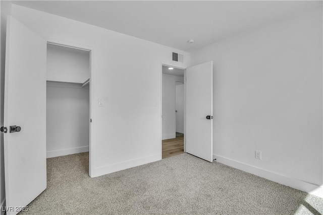 unfurnished bedroom with a walk in closet, baseboards, visible vents, and carpet flooring