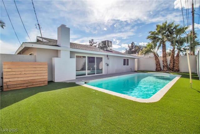 rear view of house with cooling unit, a yard, a fenced backyard, stucco siding, and a chimney