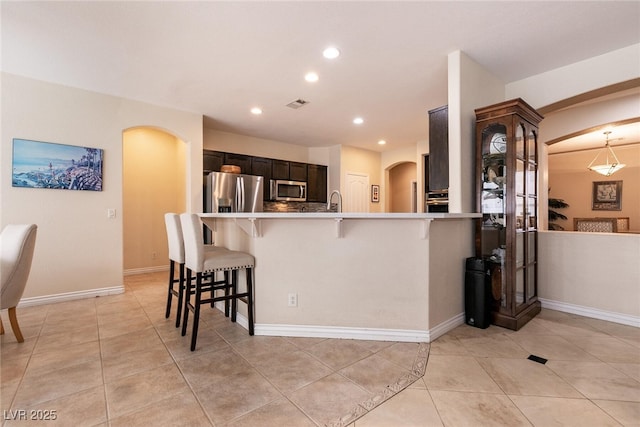 kitchen featuring visible vents, a breakfast bar, appliances with stainless steel finishes, a peninsula, and arched walkways