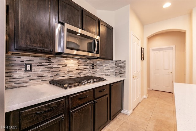 kitchen featuring light tile patterned flooring, arched walkways, stainless steel appliances, decorative backsplash, and light countertops