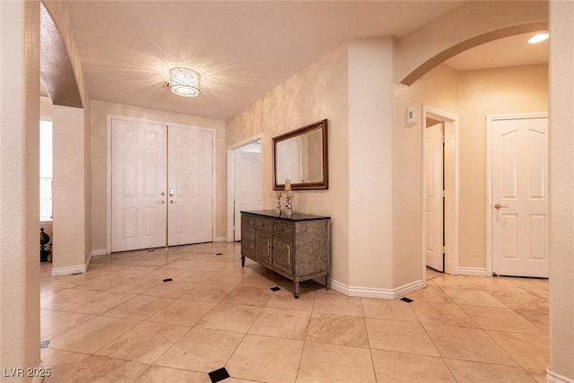 foyer entrance with baseboards, arched walkways, and light tile patterned flooring