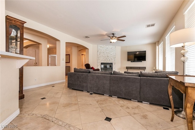 living area featuring visible vents, a ceiling fan, arched walkways, a fireplace, and light tile patterned floors