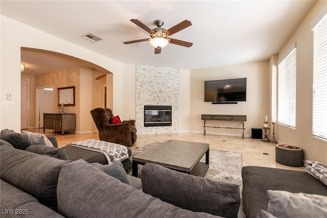 living area with visible vents, arched walkways, a stone fireplace, baseboards, and ceiling fan