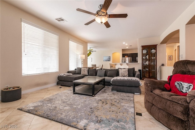 tiled living room featuring visible vents, arched walkways, baseboards, and ceiling fan