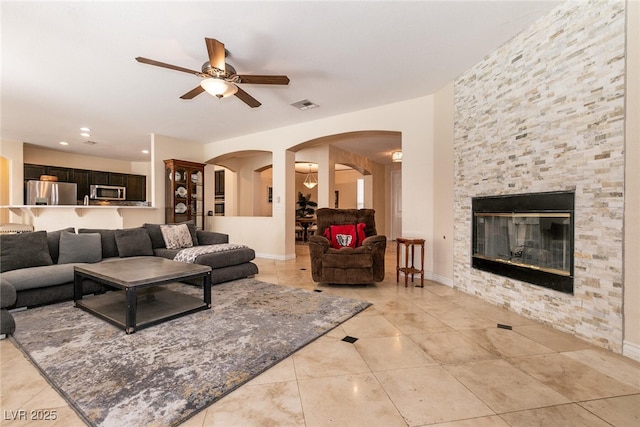 living room featuring visible vents, arched walkways, a fireplace, baseboards, and ceiling fan