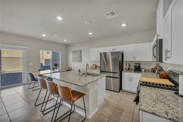 kitchen with visible vents, a breakfast bar area, appliances with stainless steel finishes, white cabinetry, and a sink