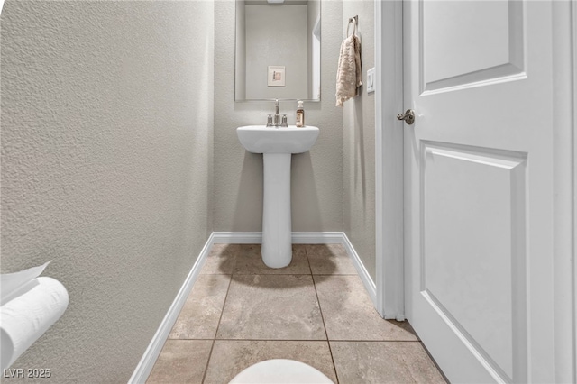 bathroom featuring tile patterned floors, a textured wall, and baseboards