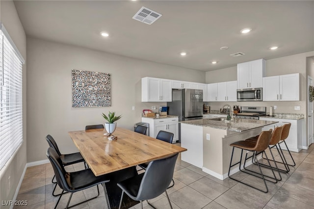 kitchen with visible vents, a center island with sink, appliances with stainless steel finishes, a breakfast bar area, and white cabinets