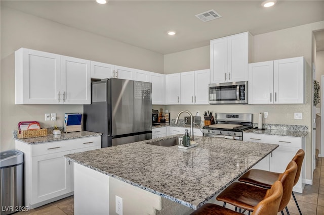 kitchen featuring visible vents, a breakfast bar, appliances with stainless steel finishes, white cabinets, and a sink