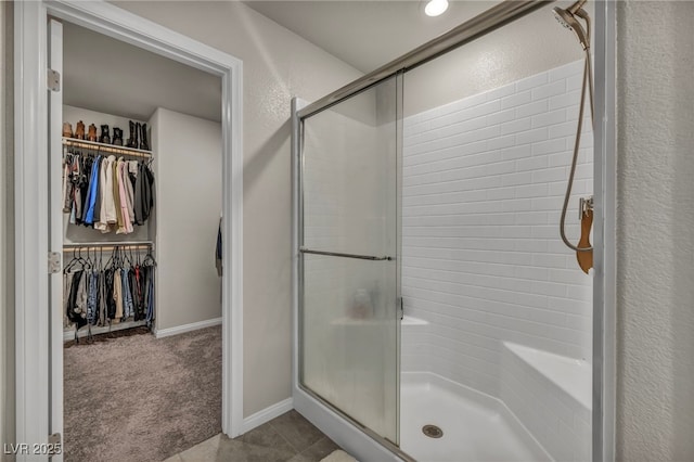 full bath with baseboards, a spacious closet, a shower stall, and a textured wall