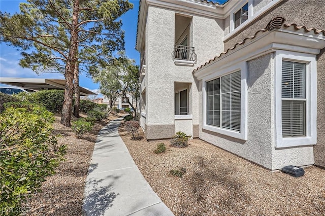 view of side of home featuring a tiled roof, a balcony, and stucco siding