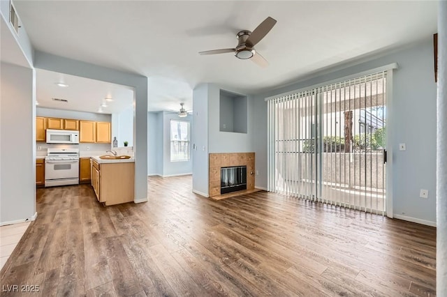 unfurnished living room with a sink, baseboards, ceiling fan, and dark wood finished floors