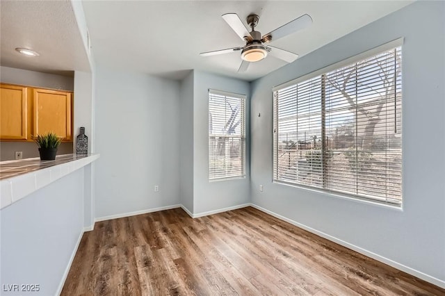 unfurnished dining area featuring wood finished floors, baseboards, and ceiling fan