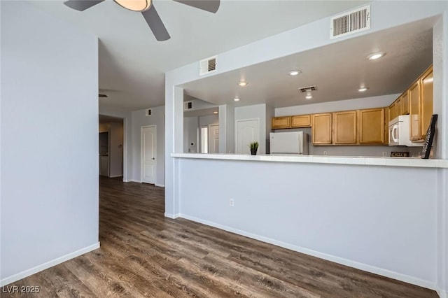 kitchen featuring white appliances, tile counters, a ceiling fan, and visible vents