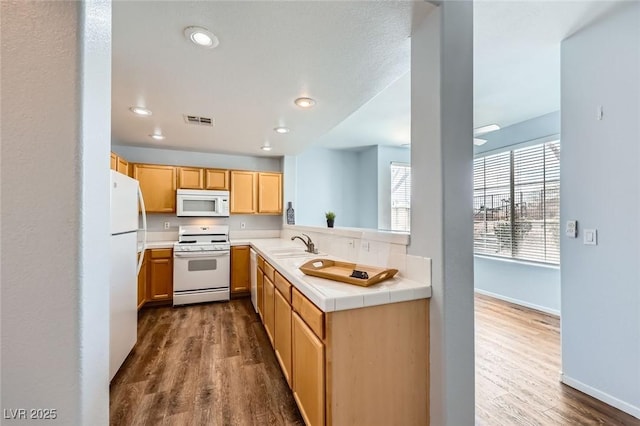 kitchen featuring white appliances, visible vents, a sink, tile counters, and dark wood-type flooring