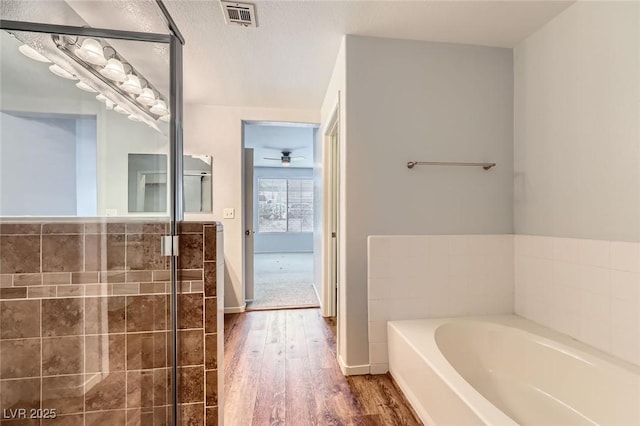 bathroom with a garden tub, wood finished floors, visible vents, and ceiling fan