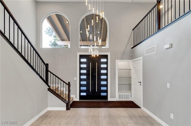 entryway with visible vents, wood finished floors, and a towering ceiling