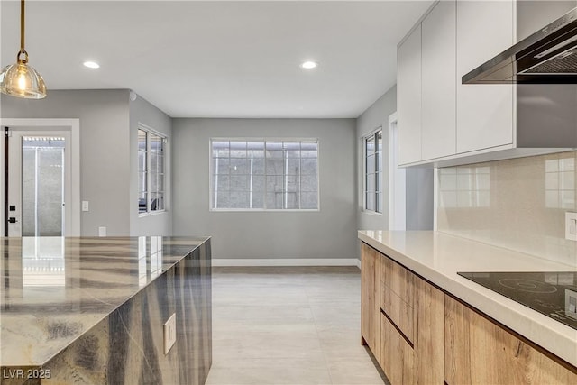 kitchen with pendant lighting, baseboards, modern cabinets, and wall chimney exhaust hood